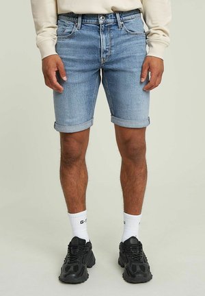 Lichtblauwe denim shorts met een opgerolde zoom, vijf zakken en een klassieke rits. Gepaard met zwarte sneakers en witte sokken.