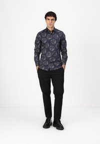 Skjorte med knapper i mørkeblå bunn og blomstermønster i gråtoner; kombinert med svarte bukser og svarte sko. Teksturert stoffdetalj synlig.
