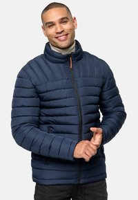 Navy blue puffer jacket with horizontal quilted design, high collar, front zipper, and side pockets. Fabric appears smooth and insulated.