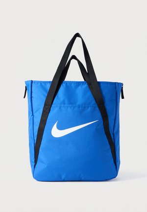 Niebieska torba na ramię z nylonu z czarnymi paskami, z dużym białym logo Nike w kształcie znaku Swoosh. Górne zamknięcie na zamek oraz dodatkowa kieszeń z boku.
