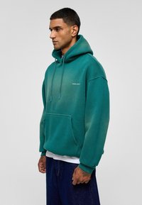 Hoody in een verloop van teal, van een katoenmix. Beschikt over een grote zak aan de voorkant, een trekkoord en een logo op de borst. Losse pasvorm met geribbelde mouwen.