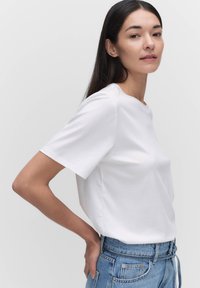 Biała bawełniana koszulka z krótkim rękawem i okrągłym dekoltem, noszona z jasnoniebieskimi dżinsami z wysokim stanem. Gładka tekstura, minimalistyczny design.