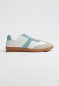 Zapatilla blanca con detalles en azul claro y suela de goma beige. Parte superior sintética suave, con costuras rectas y punta redondeada.