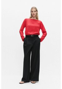 Punainen satiininen pitkähiha blouse suoran leikkauksen kanssa, yhdistettynä korkeavyötäröisiin mustiin leveälahkeisiin housuihin. Asusteet sisältävät mustan vyön.