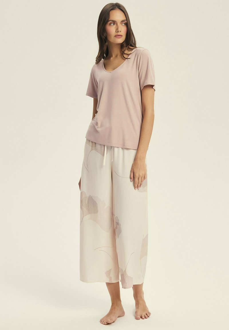 Jasno różowa koszulka z dekoltem w kształcie litery V w połączeniu z kremowymi spodniami w szerokim kroju, zdobionymi floralnym wzorem w delikatnych odcieniach taupe i różu. Miękki, lejący się materiał.