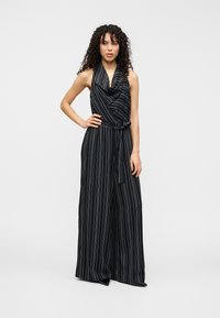 Combinaison rayée noir et blanc avec un col bénitier et des jambes larges ; elle est dotée d'une ceinture à nouer à la taille pour un ajustement optimal.