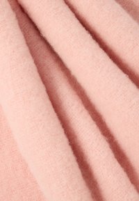 Růžová vlněná tkanina s měkkým, texturovaným povrchem, vykazující světlý růžový odstín a lehce chlupatý vzhled. Více záhybů vytváří hloubku.