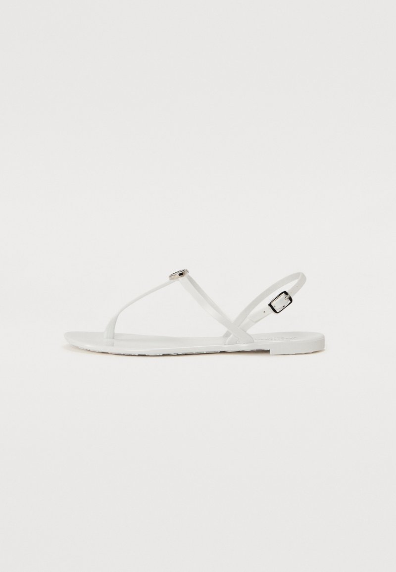 Sandales plates blanches au design minimaliste, avec de fines lanières, une petite boucle décorative et une semelle lisse et plate.