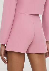Pantaloni corti rosa su misura con una texture liscia, caratterizzati da una vita alta e linee pulite. Il design è minimalista, senza chiusure visibili.