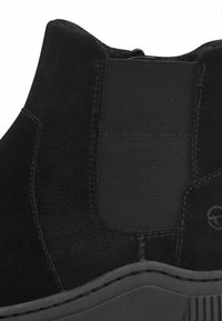 Bottines en daim noir avec un panneau élastique côtelé, une semelle texturée et des coutures détaillées le long des bords.