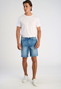 Biała koszulka z krótkim rękawem w połączeniu z jasnoniebieskimi szortami dżinsowymi, posiadającymi prosty krój i wykończenie, uzupełniona białymi sneakersami.