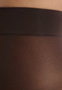 Brązowe zarówno nieprzezroczyste rajstopy z gładką teksturą, z szerokim brązowym pasem, przechodzącym w przezroczystą część nogi.