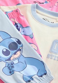 Tri dijela dječje odjeće s likom Stitča iz Disney-a. Kombinacije ružičaste i plave boje, s printanim likovima i mekanim teksturama tkanine.