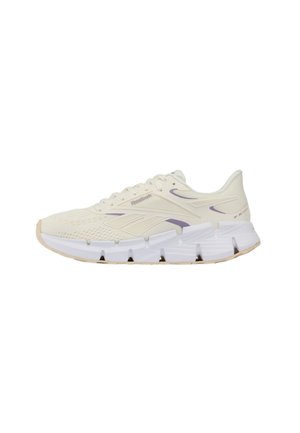 Chaussure de course Reebok beige clair avec semelle blanche segmentée et accents de logo violets, positionnée de côté sur un fond blanc.