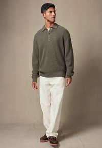 Strikket olivengrønt pullover-sweater med krave og tre knapper, parret med cremede bukser og brune snørebåndssko.