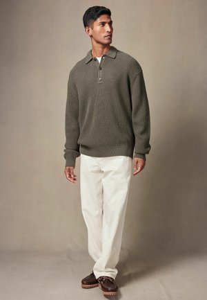 Olivgrüner Strickpullover mit Kragen und drei Knöpfen, kombiniert mit cremefarbenen Hosen und braunen Schnürschuhen.