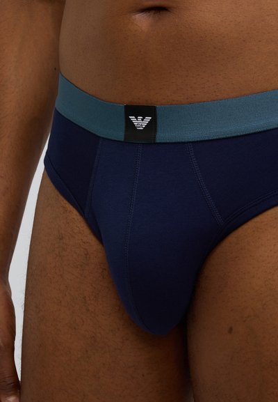 Vyriškos trumpikės tamsiai mėlynos spalvos, pagamintos iš minkštos medžiagos, su kontrastinga žalsvai mėlyna elastinga juosmens juosta ir juodu logotipo lipduku.