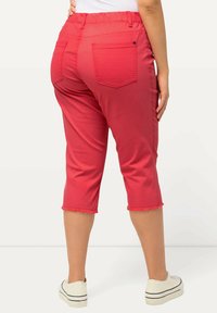 Rode cropped broek met een elastische taille, voorzien van twee achterzakken en franjes langs de zoom. Gecombineerd met witte sneakers.