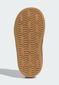 Hnedá gumená podrážka tenisky s vlnitým dezénom a vyvýšenými časťami. Obsahuje embosované logo v blízkosti oblasti päty.