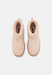 Beige fuzzy ankle boots with a soft texture, elasticized collar, and a tan rubber sole. The interior features a plush lining for comfort.