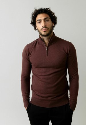 Burgunderfarbenes Langarmshirt mit einem Viertelreißverschluss-Kragen, aus einem glatten Material gefertigt. Es hat eng anliegende Ärmel und einen gerippten Saum.