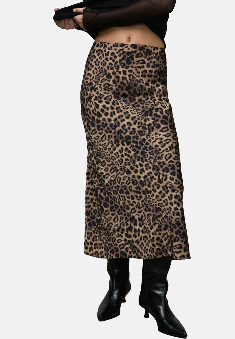 Spódnica midi w panterkę w beżowym i czarnym kolorze, o prostym kroju i subtelnym połysku, zestawiona z czarnymi botkami na obcasie.