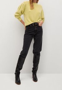 Helles gelbes Strickpullover mit Puffärmeln, kombiniert mit hochgeschnittenen schwarzen Jeans und schwarzen kniehohen Lederstiefeln.