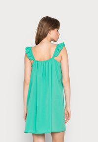 Um vestido solto, sem mangas, na cor turquesa vibrante, com alças franzidas e uma textura suave, caindo acima do joelho com detalhes plissados.