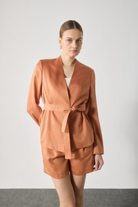 Burnt orange blazer with a tie belt, paired with matching shorts. Smooth fabric with a slightly shiny texture, featuring a shawl collar.
