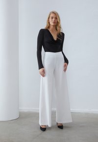 Must mustre with drape kaelus, mis on paaritatud kõrge vöökohtadega valgete laiade pükstega. Mustad terava ninaga kontsad lõpetavad riietuse.