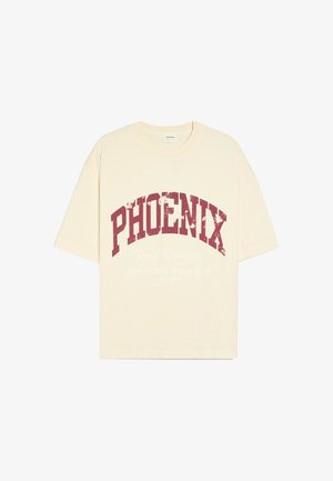 Personne portant un t-shirt blanc Phoenix et un jean foncé, en équilibre sur le bord d'une piscine ronde dans un jardin avec des arbres et des buissons.