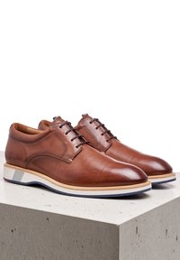 Des chaussures en cuir marron présentent un design épuré, des orteils ronds et une semelle blanche contrastante avec des accents bleus. Les lacets permettent un ajustement réglable.