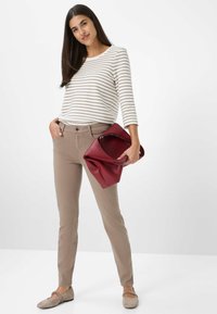 Gestreiftes Langarmhemd in Weiß und Beige, beige Hosen und eine rote Lederhandtasche mit einem weichen, gefalteten Design. Bequeme flache Schuhe runden den Look ab.