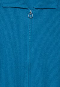 Tyrkysový svetr s texturovaným žebrovaným designem, s centrálním stříbrným zipem a obdélníkovým límcem. Měkký pletený materiál.