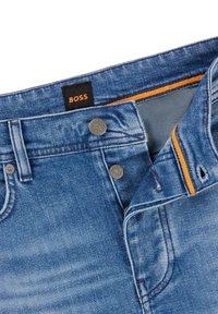 Blå denimjeans med metallknappar, orange detaljer inuti midjebandet och en svart etikett med orange "BOSS"-text.