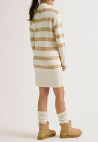Robe-pull rayée crème et beige, ourlet côtelé, associée à des bottines marron clair et des jambières blanches côtelées. Texture douce en maille.