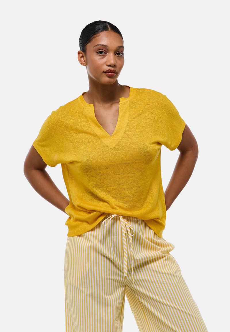 Haut jaune en lin à manches courtes avec un décolleté en V, associé à un pantalon rayé blanc et jaune. Matériau léger, légèrement texturé.