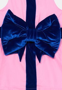 Tissu rose avec un grand nœud en velours bleu foncé à l'arrière, présentant une texture satinée et une finition lisse. Accent de ruban bleu vertical.