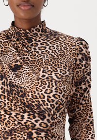 Top med leopardmönster med hög krage, mjukt tyg och rynkdetaljer på axlarna. Rika nyanser av ljusbrunt och svarta mönster.