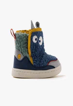 Botas infantiles coloridas hechas de materiales multi-texturizados. Presentan secciones en azul, verde y gris, con detalles de ojos y orejas juguetonas.
