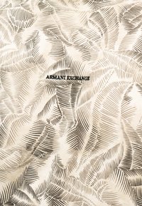 Μπεζ ύφασμα με αφηρημένα σκούρα καφέ φύλλα και το λογότυπο «ARMANI EXCHANGE» κεντημένο με μαύρο στο κέντρο.