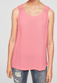 Top sin mangas rosa con detalles texturizados en los hombros, escote redondo y un ajuste relajado, combinado con jeans de mezclilla desgastados.