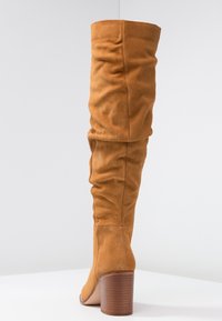 Botas altas y holgadas hasta la rodilla, hechas de ante en tono beige, con un tacón de madera ancho y una textura suave, sin adornos ni patrones.