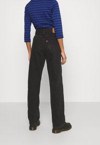 Pantalones vaqueros anchos y negros con cintura alta, con bolsillos traseros y una etiqueta de cuero. Combinados con una camisa a rayas azul y negra y botas negras.