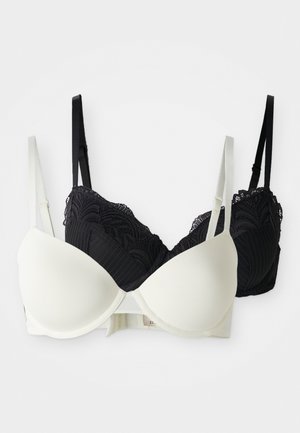Two bras displayed together; one in white smooth fabric and the other in black lace with ribbed texture, featuring adjustable straps.