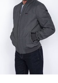 Blouson aviateur gris à carreaux avec une fermeture éclair à l'avant, des poignets et une taille côtelés. Présente un logo subtil sur la poitrine et des poches sur les côtés.