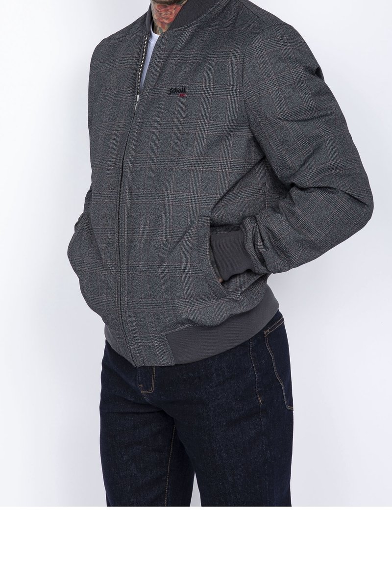 Blouson aviateur gris à carreaux avec une fermeture éclair à l'avant, des poignets et une taille côtelés. Présente un logo subtil sur la poitrine et des poches sur les côtés.