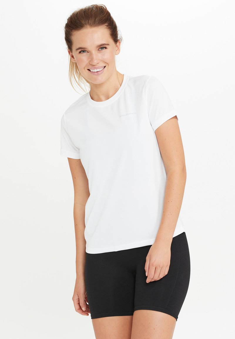 Vit kortärmad t-shirt i ett mjukt, lätt material, med en diskret logotyp nära axeln. T-shirten är kombinerad med svarta shorts.