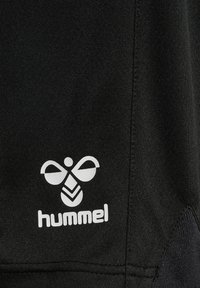 Svart atletisk tyg med en vit logotyp av en bi med stiliserade vingar och ordet "hummel". Texturerad yta med sömmar synliga.