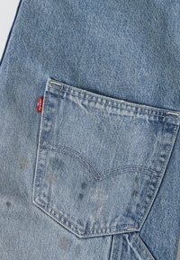 Πίσω τσέπη ανοιχτό μπλε τζιν Levi's με ορατές ραφές και κόκκινη ετικέτα Levi's στην πλευρά της τσέπης.